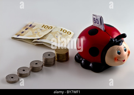 Un salvadanaio a forma di una coccinella con moneta danese intorno. isolato su sfondo chiaro Foto Stock