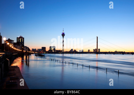 Dusseldorf cityscape con la passeggiata sul lungofiume del Reno, Torre sul Reno, ponte Rheinknie, MediaHarbor, stagliano tramonto, alta marea Foto Stock