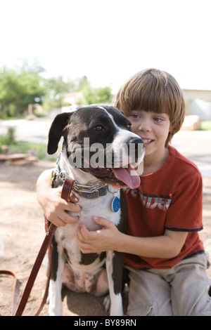 A sette anni di vecchio ragazzo abbraccia il suo pit bull outoodrs. Foto Stock