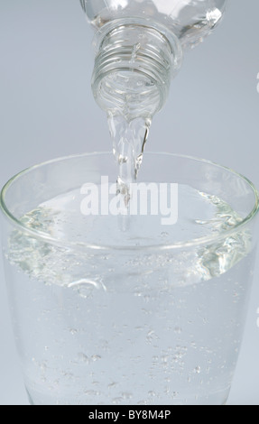 Acqua dalla bottiglia essendo versata in un bicchiere Foto Stock