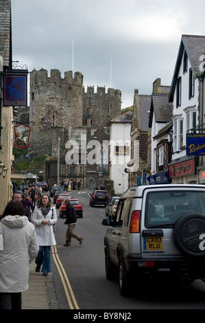 La strada principale dello shopping a Conwy, il Galles del Nord, con il castello in background. Foto Stock