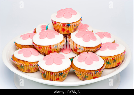 Pila di piccoli cupcakes, noti anche come panini, con glassa bianca decorata con fiori rosa fondente. Foto Stock