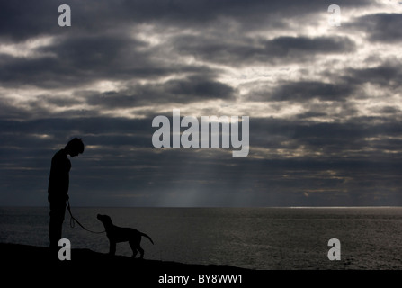 Ragazzo e cane singolo ragazzo adolescente con labrador cucciolo Silhouette Chesil Beach, Dorset, Regno Unito Foto Stock