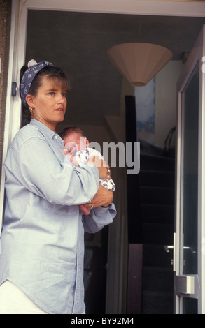 Infelice madre in piedi a porta aperta mentre tiene il suo bambino Foto Stock