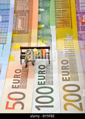 Varie banconote in euro con una miniatura la figura di una persona senza dimora su una panchina nel parco, immagine simbolica di euro-crisi Foto Stock
