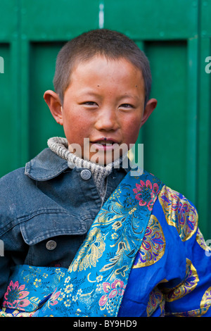 Moderno e giovane ragazzo tibetano indossando giacca denim sovrastata da colorati in oro e seta ricamata anta. JMH4649 Foto Stock