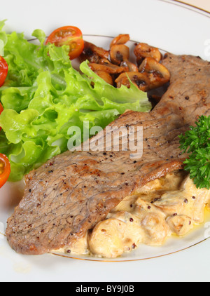 Scaloppine su un letto di funghi in una crema e salsa di aglio, servito con lattuga, pomodori ciliegini e funghi fritti Foto Stock