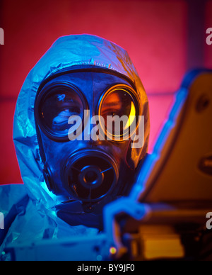 Uomo che indossa una faccia maschera a gas vestito in una guerra chimica suit usando un computer portatile Foto Stock