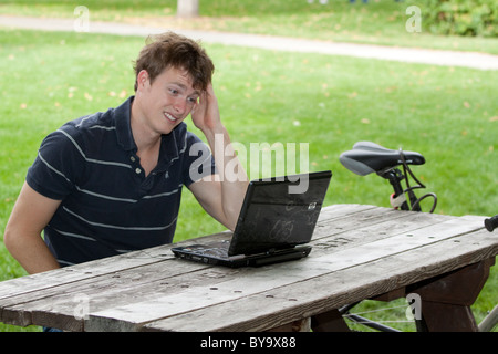 Maschio giovane studente di college reagisce a qualcosa che egli sta leggendo sul suo computer portatile Foto Stock