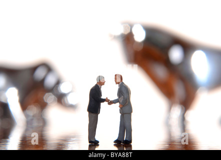 Due manager figurine stringono le mani, con bull e bear fuori fuoco dietro di loro, immagine simbolica per stock exchange business Foto Stock