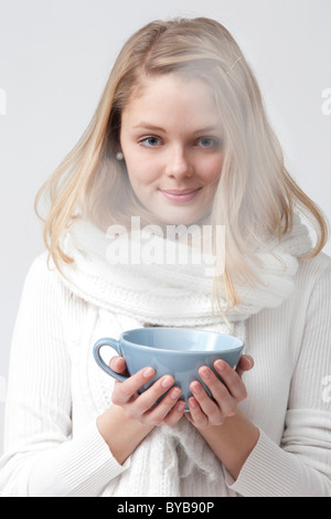 Giovane donna vestita di bianco tenendo una tazza di tè con entrambe le mani Foto Stock