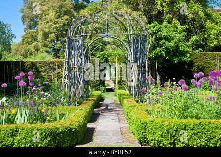 Un sentiero lastricato sotto un pergolato o pergolato con scatola bedds coperto intorno in un paese di lingua inglese giardino d'estate. Foto Stock