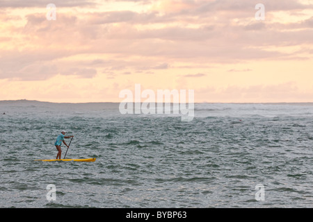 Racchetta imbarco in Hanalei Bay al tramonto. Un lone paddler ventures fuori verso la superficie ruvida della baia. Foto Stock