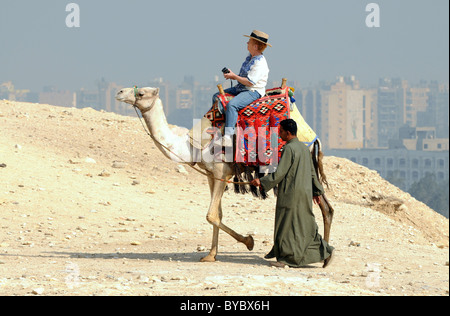 L'Egitto, i turisti a cavallo di cammelli di Giza in Egitto con la città del Cairo in background. Foto Stock