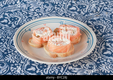 Salmone affumicato arrotolate intorno il formaggio e le erbe ripieno su pane francese tostato antipasti su una piastra Foto Stock