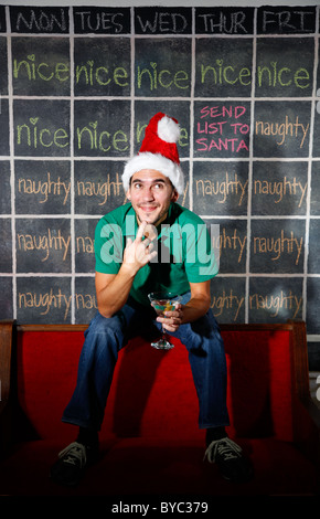 Uomo con elf hat sorridere di fronte naughty e Nizza dicembre Natale calendario con un martini in mano. Foto Stock