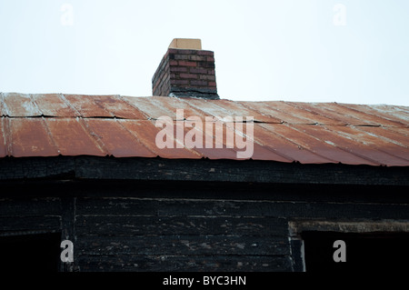 Un arrugginito tetto stagno su un vecchio bruciate-down home. Foto Stock