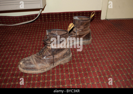 In pelle indossato stivali da lavoro sul pavimento di una brutta roach motel. Foto Stock