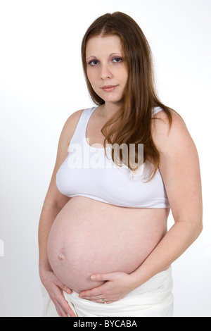 Una giovane donna incinta trattiene il suo ventre gonfio di indossare un reggiseno per lo sport. Foto Stock