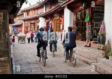 Tre uomini in bicicletta attraverso una stretta corsia pavimentata a Lijiang old town, nella provincia dello Yunnan in Cina. JMH4755 Foto Stock