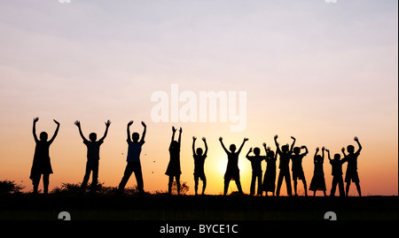 Silhouette Indian ragazze e ragazzi saltando e agitando in piedi su un riso risaie al tramonto. Andhra Pradesh, India Foto Stock