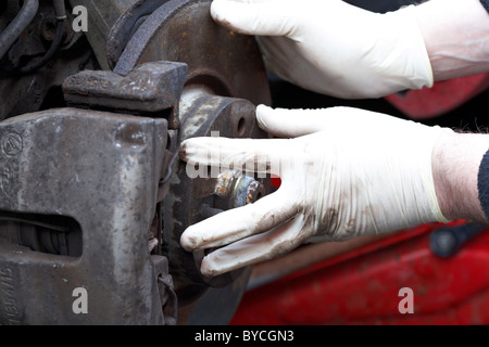 Mechanic indossando guanti di gomma di eseguire la manutenzione dell'automobile su un vecchio arrugginito del mozzo della ruota Foto Stock