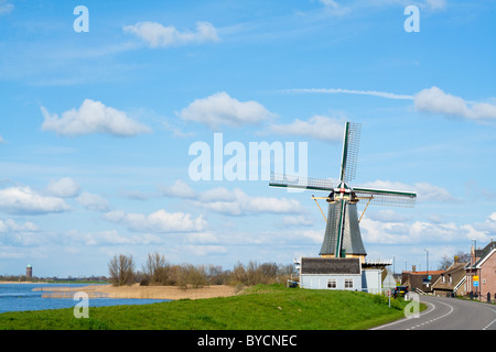 Piccola cittadina olandese accanto a una diga con canal e mulino a vento Foto Stock