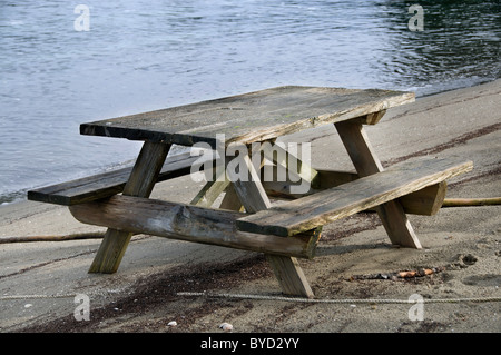 Un vuoto che alterò picnic in legno tavolo siede sul bordo dell'acqua in una posizione tranquilla vicino a Olympia, Washington. Foto Stock