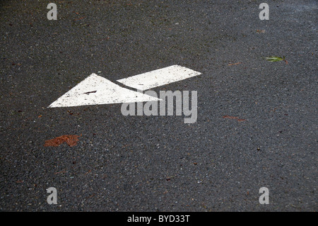 Una freccia bianca dipinta su asfalto di punti in una direzione. Foto Stock