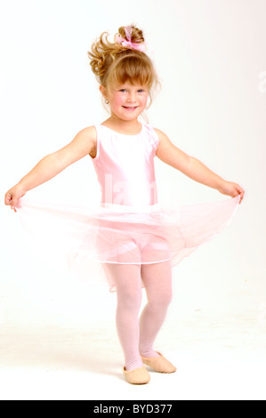 Poco sorridente bambina indossa un balletto di rosa vestito è ballare tenendo il suo abito Foto Stock