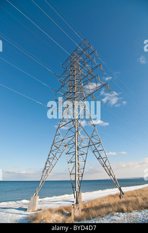 Una trasmissione elettrica porta torre di linee ad alta tensione accanto a un lago in inverno. Foto Stock