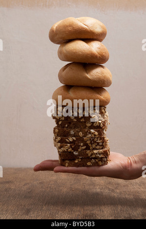 Mano che tiene una pila di rotoli di pane e fette di pane Foto Stock