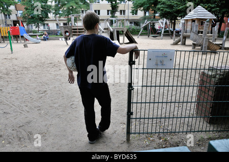 Ragazzo solitario, 10 anni, all'entrata di un parco giochi, Colonia, nella Renania settentrionale-Vestfalia, Germania, Europa Foto Stock