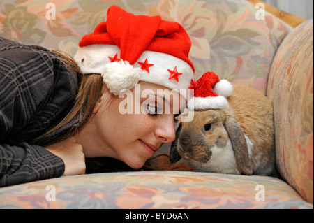 Giovane donna con una nana lop bunny o coniglio (oryctolagus cuniculus), indossando cappelli di Babbo Natale, amore per gli animali Foto Stock
