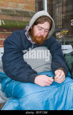 , Londra Liverpool Street Station , rosso intitolata & barbuto giovani senzatetto uomo avvolto nel sacco a pelo fumatori - ventole di 2 anni Foto Stock