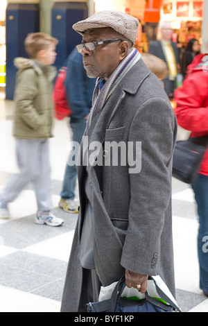 , Londra Liverpool Street Station , si chinò nero anziani afro-caraibica uomo , il tappo piatto , occhiali & cappotto invernale passeggiate causeway Foto Stock