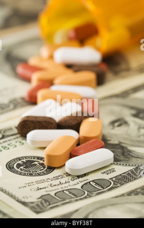 Una varietà di pillole e vitamine fuoriuscito da una bottiglia di colore arancione su American $100 fatture del dollaro. Foto Stock