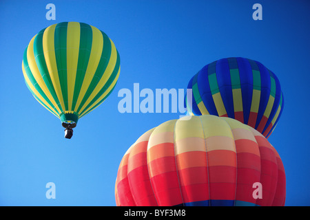 3 colorate mongolfiere pigramente flottante di distanza su un vibrante blu cielo. Foto Stock