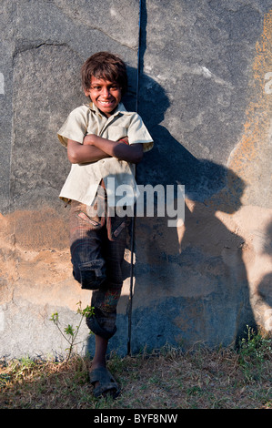Felice giovani poveri di casta inferiore Indian street boy sorridente appoggiato contro una parete di pietra. Andhra Pradesh, India Foto Stock