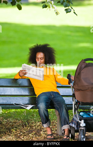 Giovane uomo con carrello bambino seduto sul banco e quotidiano di lettura Foto Stock