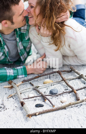 Metà adulto giovane gioca tic-tac-punta sulla spiaggia, vicino a baciare Foto Stock