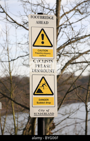 Un metallo cartello di avviso su un sentiero pubblico la consulenza di un ponte a monte e a un calo improvviso, Sunderland, England, Regno Unito Foto Stock