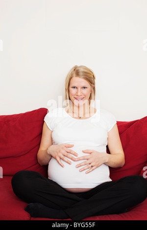 Ritratto di donna incinta toccando lo stomaco sul divano Foto Stock