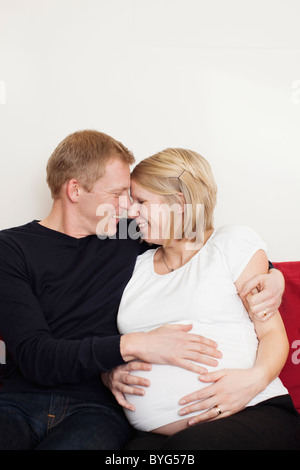 Il marito con la moglie incinta seduti sul divano e guardando ogni altro Foto Stock