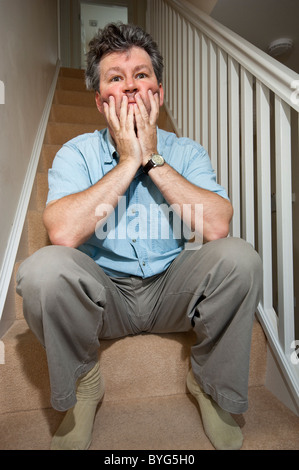 Uomo di mezza età depressa triste lonely pensando scarsamente stanco infelice da solo singole scale all'interno di casa angst depressione emo Foto Stock