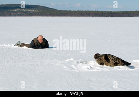 L uomo giace sulla neve e guarda alla guarnizione inanellato vicino a ice-foro. Guarnizione Jar, netsik o nattiq (Pusa hispida), Mare Bianco, artiche, Russia Foto Stock