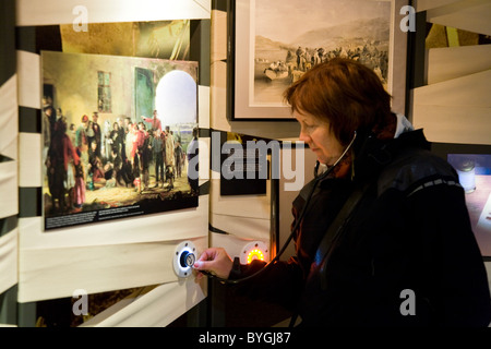 Tourist indossando 'stethoscope' le cuffie / cuffie audio guida guardando un display. Florence Nightingale Museum. Londra. Regno Unito. Foto Stock