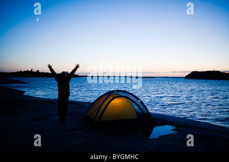 Persona vicino a tenda illuminata dal mare al crepuscolo Foto Stock