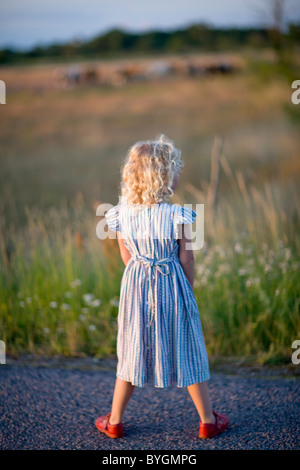 Ragazza in piedi sulla strada rurale, vista posteriore Foto Stock