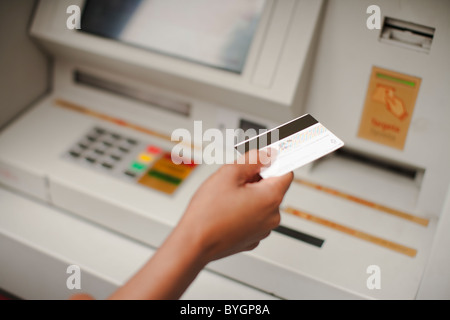 Mano umana tenendo la carta di credito, bancomat in background Foto Stock